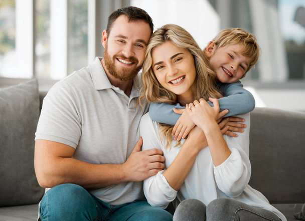 Happy caucasian family of three looking relaxed while sitting and bonding on the sofa together. Adorable little blonde boy chilling on a couch with his loving parents while hugging them. - Fotografie, Obrázek