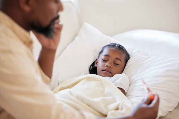 Kranke Afroamerikanerin liegt schlafend zu Hause im Bett. Besorgter Vater ruft Arzt, um seiner kranken Tochter zu helfen, nachdem er ihre hohe Körpertemperatur mit Thermometer auf Fiebersymptome überprüft. - Foto, Bild