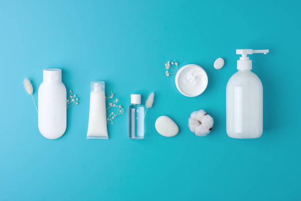 Composición cosmética con productos cosméticos para el cuidado de la piel y flores sobre fondo azul. Colocación plana, espacio de copia  - Foto, imagen