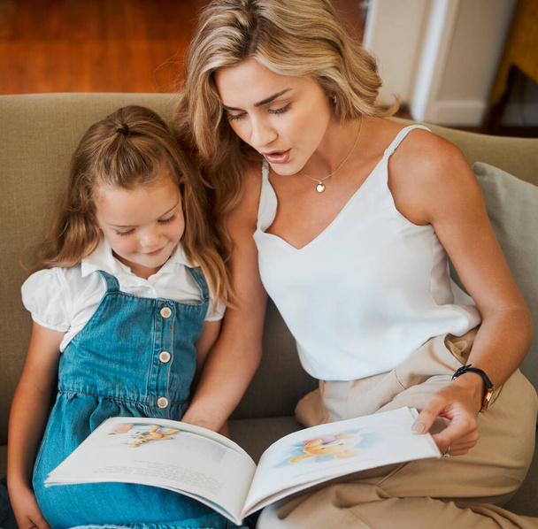 若いコンテンツの原因アジアの母親と小さな娘が一緒に自宅でソファに座って物語本を読んでいます。お母さんと読書する気のない女の子。子供におとぎ話を読んでいる女. - 写真・画像