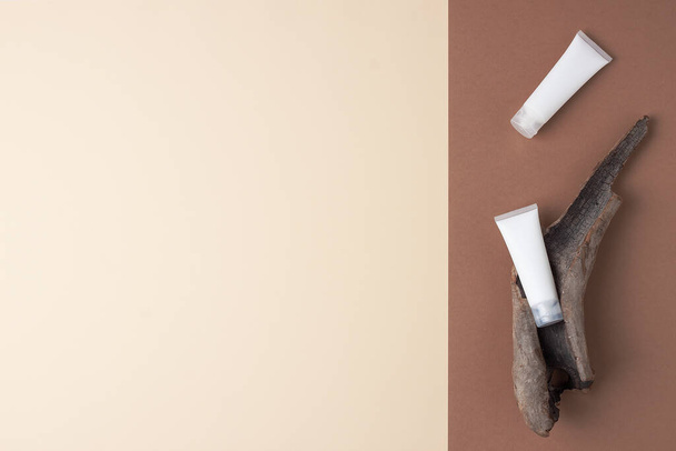 White tubes of cosmetic cream with wood on brown and beige background. Flat lay, copy space - Valokuva, kuva