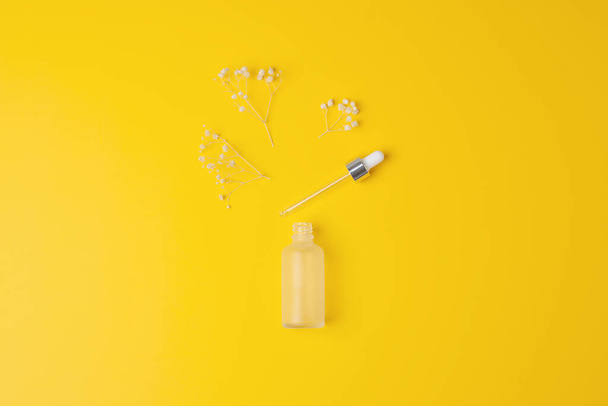Sarı arka planda çiçekler olan kozmetik şişesi. Düz yat, boşluğu kopyala - Fotoğraf, Görsel