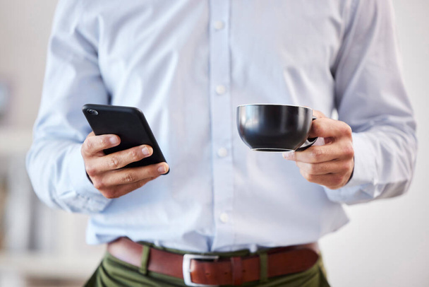 Closeup of male hands holding coffee and smartphone. Businessman using mobile phone to send text, browse social media or use app while on his tea break. - Foto, imagen