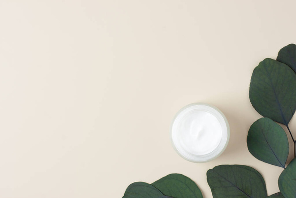 Jar of cosmetic cream with eucalyptus on pastel beige background. Flat lay, copy space - Foto, Imagem