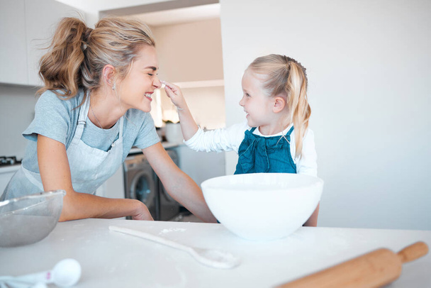 Little girl baking with her mother. Mother and daughter bonding while cooking. Little child playfully putting flour on her moms nose. Happy mother and child playing while baking together. - Foto, imagen
