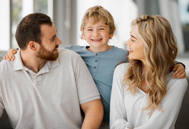 Happy caucasian family of three looking relaxed while sitting and bonding on the sofa together. Adorable little blonde boy chilling on a couch with his loving parents while hugging them. - Foto, Bild