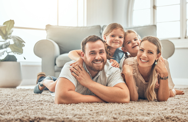 Young family in the living room at home. Portrait of an affectionate and happy family lying on the floor of the lounge. Spending quality time together. A mother, father and two sisters at home. - Foto, Imagen