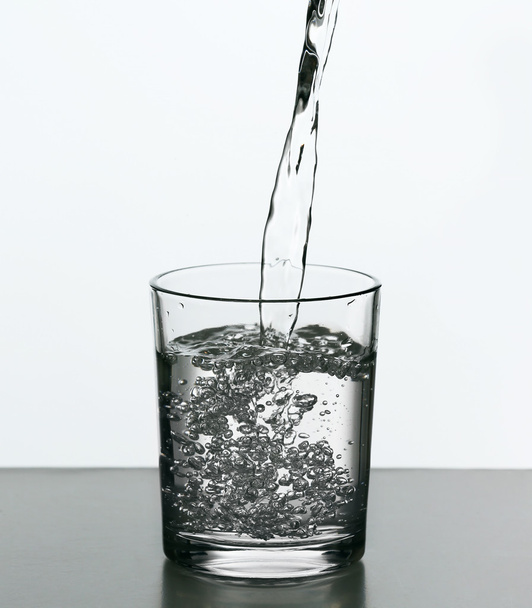 白で隔離ガラスのボトルから水を注ぐ - 写真・画像