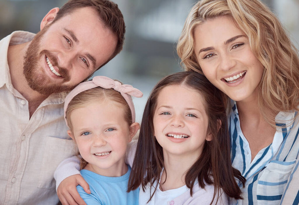 Portrait of happy young caucasian family sitting together in the living room smiling with healthy teeth at home. Adorable little girls hugging their mom and dad. Carefree parents and their two daught. - Foto, Imagem