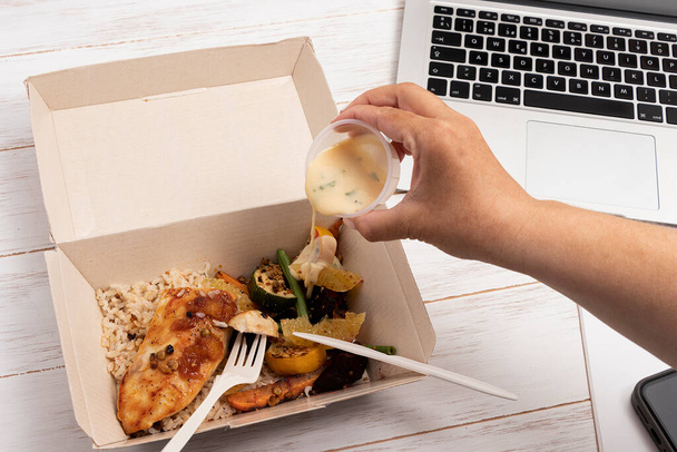 Человек кладет соус на обед с курицей и рисом в экологическую коробку для доставки - Фото, изображение