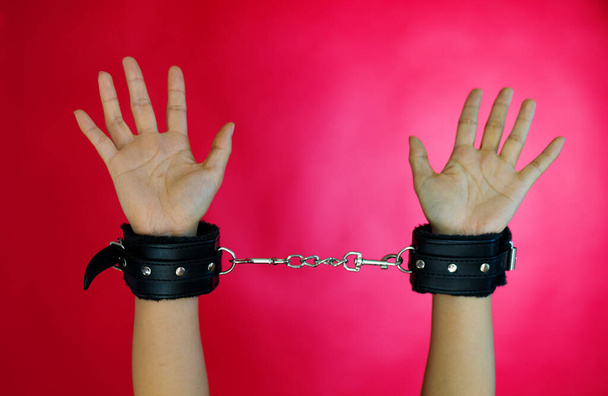 cropped shot of woman in erotic play with black leather handcuffs on red background. - Photo, Image