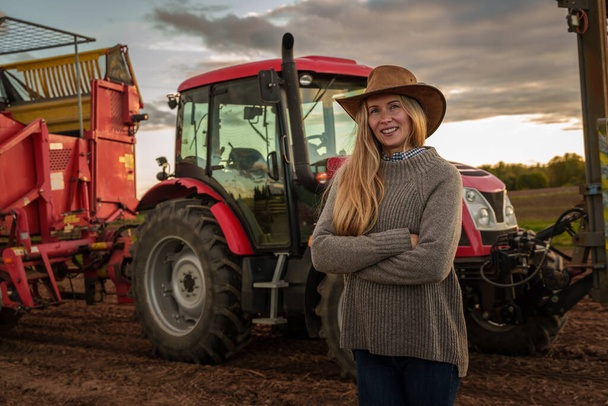 Portrait of confident farmer woman and modern combine on cultivated field. - Photo, Image