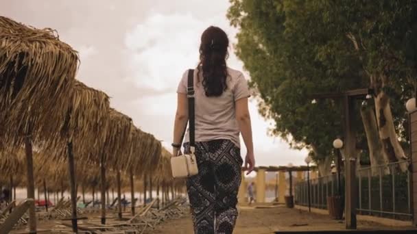 Frau spaziert auf Holzweg ans Meer vorbei an Sonnenschirmen und Liegestühlen. Hochwertiges 4k Filmmaterial - Filmmaterial, Video