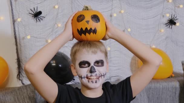 Ένα χαρούμενο παιδί με μακιγιάζ με τη μορφή σκελετού και κολοκύθας στο κεφάλι γιορτάζει το Χάλογουιν. Ημέρα των Αγίων Πάντων τον Οκτώβριο - Πλάνα, βίντεο