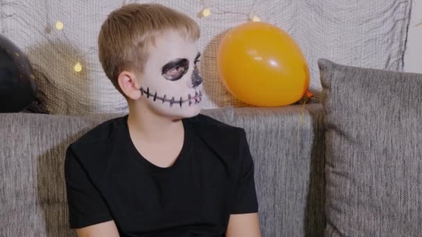 Κοντινό πορτραίτο ενός αγοριού με μακιγιάζ στο πρόσωπό του με τη μορφή σκελετού για το Χάλογουιν. Παιδί είναι έτοιμο για το κόλπο ή τη θεραπεία των διακοπών. - Πλάνα, βίντεο