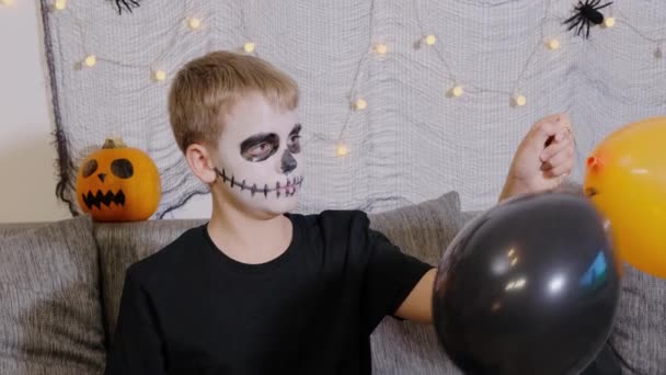 Chłopiec jest udekorowany jako szkielet świętujący Halloween balonami. Chłopiec jest urządzony jako szkielet świętujący Halloween z balonami w domu. Dzień Wszystkich Świętych - Materiał filmowy, wideo