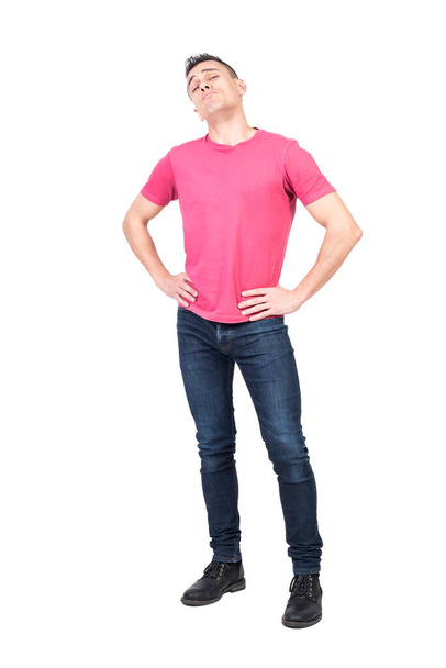 Selbstbewusster Mann in Jeans und rosa T-Shirt hält die Hände auf der Taille und blickt mit stolzem Gesichtsausdruck isoliert auf weißem Hintergrund in die Kamera - Foto, Bild