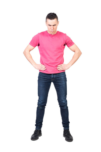 Full length of confident annoyed male model with dark hair in casual outfit looking at camera with serious face expression while standing against white background with hands on waist - Foto, imagen