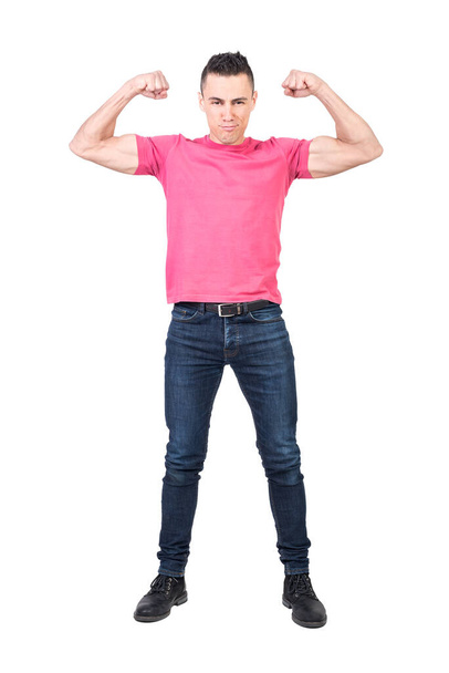 Full body of young self assured muscular male model in pink t shirt and jeans showing biceps and looking at camera isolated on white background - 写真・画像