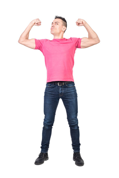 Plná délka mladý silný mužský model s tmavými vlasy v ležérní oblečení ukazující biceps a při pohledu na kameru s jistotou proti bílému pozadí - Fotografie, Obrázek
