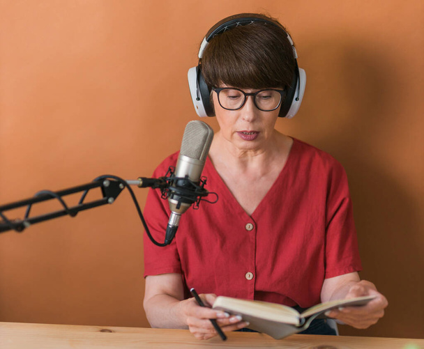 Portrait of mature woman wearing headphones and talking at online radio station - podcast and broadcast - Fotografie, Obrázek