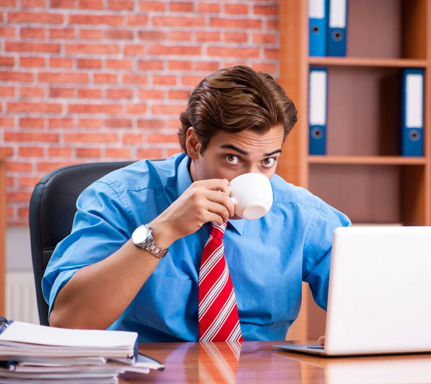 Mladý zaměstnanec s nadměrnou prací sedí v kanceláři - Fotografie, Obrázek