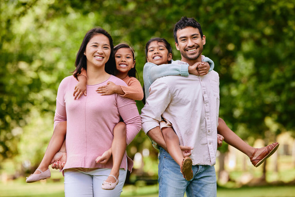 Portret szczęśliwej azjatyckiej rodziny stojącej blisko siebie w parku. Urocze dziewczynki cieszące się wolnym czasem z matką i ojcem w weekend na zewnątrz. Uśmiechnięta mieszana para rasowa obejmująca. - Zdjęcie, obraz