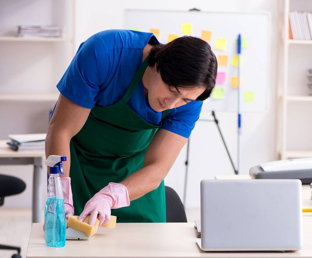 Die männliche hübsche professionelle Reinigungskraft bei der Arbeit im Büro - Foto, Bild