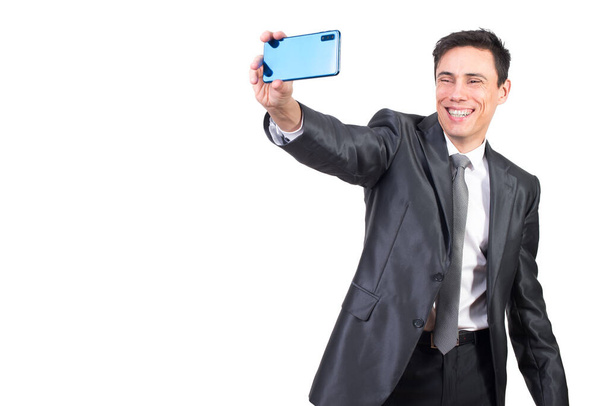 Happy male in formal suit smiling while taking self portrait on modern smartphone while standing isolated on white background in studio - Valokuva, kuva