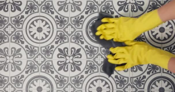 Primer plano de una persona que usa guantes amarillos limpiando un suelo de baldosas. - Metraje, vídeo