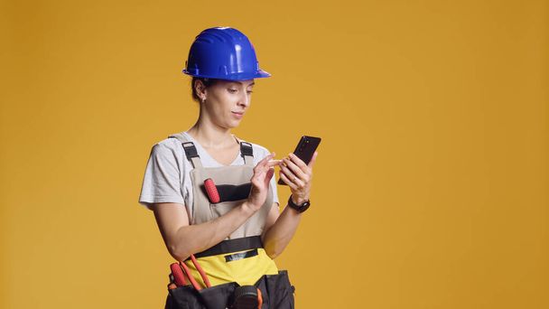 Portret kobiety inżyniera za pomocą smartfona do przeglądania Internetu i znaleźć inspirację renowacji. Pewna siebie osoba z nietypowym poczuciem siły roboczej w wyniku prac dekonstrukcyjnych. - Zdjęcie, obraz