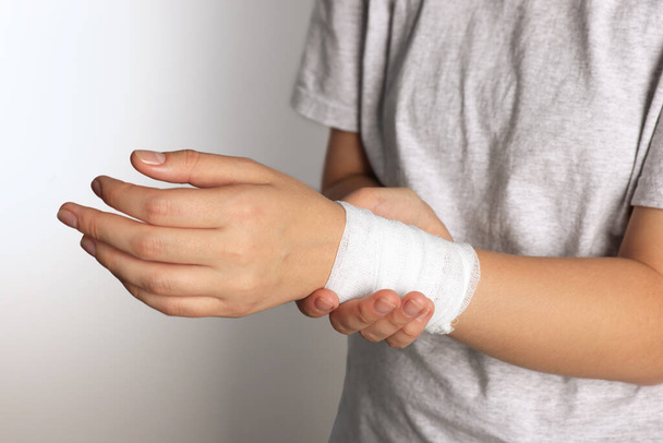 Femme avec poignet enveloppé dans un bandage médical sur fond gris clair, gros plan - Photo, image