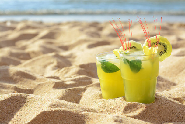 Glasses of refreshing drink with kiwi and mint on sand near sea. Space for text - Φωτογραφία, εικόνα