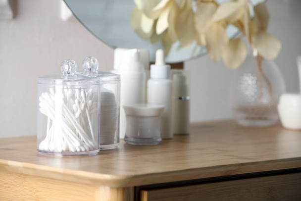 Containers with cotton swabs and pads near cosmetic products on dressing table - Фото, изображение