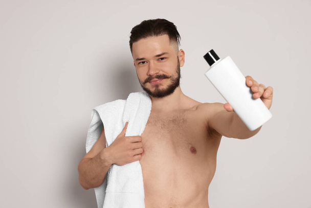 Naked man with towel and bottle of shampoo on light grey background - Foto, imagen