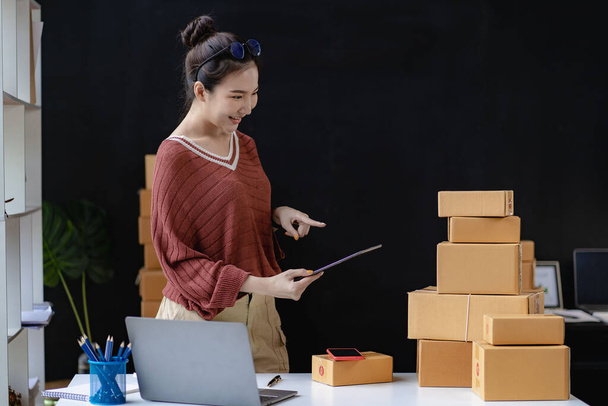 Beautiful Asian woman selling online using phone and laptop, female small business owner delivering parcels. Internet shopping lifestyle, e-commerce delivery service, SME business concept - Foto, Imagem