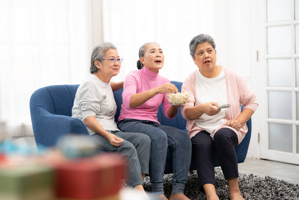 Група щасливих літніх жінок, які сидять на дивані, готові дивитися телевізор. Група азіатських літніх жінок, які проводять час у вихідні разом
.  - Фото, зображення