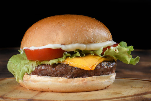 leckeres Hamburger-Sandwich mit Tomaten-Zwiebelsalat und Brot auf schwarzem Hintergrund - Foto, Bild