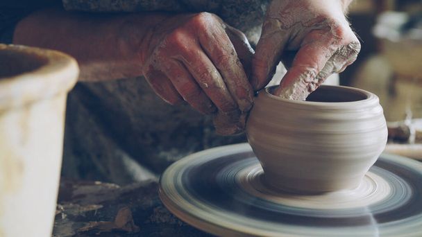 Work in pottery workshop: clay ware on throwing wheel, master ceramist molding clay using professional tools. Creating ceramic utensils and traditional occupation concept. - Foto, Imagen