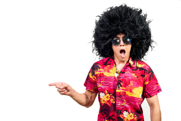 Shocked male in bright shirt with sunglasses and Afro wig looking at camera with opened mouth and looking away against white background - Photo, Image