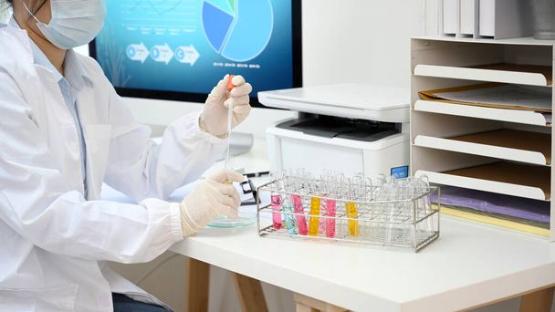 Asyalı bir kadın bilim adamı kimyasal sıvı örneklerini laboratuvar masasındaki test tüplerine yerleştiriyor.. - Fotoğraf, Görsel