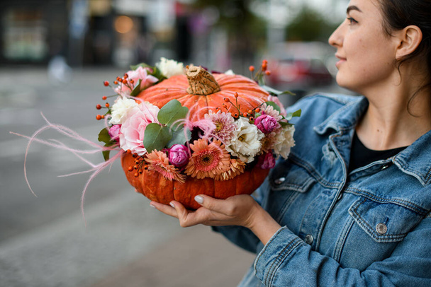 beautiful bright pumpkin with different fresh flowers inside in the hands of a young beautiful woman. Autumn bouquet - Foto, afbeelding