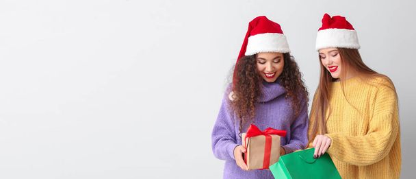 Beautiful young women with Christmas gift and shopping bag on light background with space for text - Photo, Image