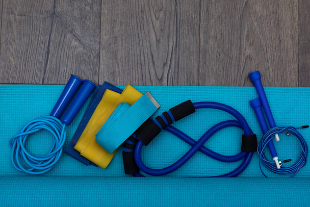 Bovenaanzicht op springtouw en fitnessband op blauwe fitnessmat op het houten oppervlak. Gezonde levensstijl en kopieerruimte, plaats voor tekstconcept - Foto, afbeelding