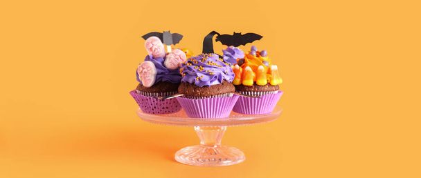 Stand with tasty Halloween cupcakes on orange background - Photo, Image