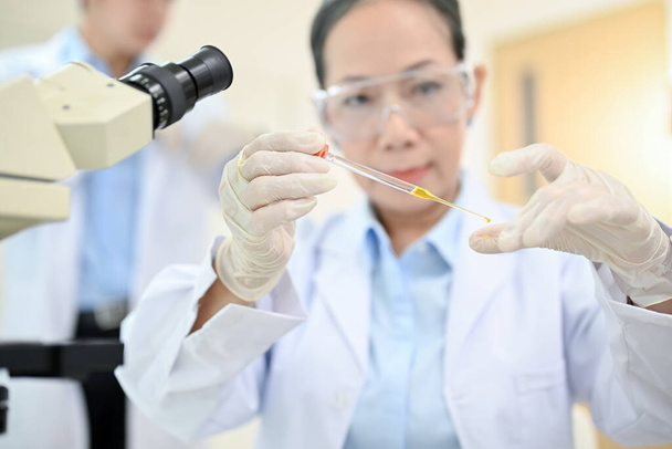 Ammattimainen aasialainen vanhempi naispuolinen tiedemies tai lääketieteellinen teknikko, joka käyttää virusnäytteen pudottamista mikroskooppiliukumäkeen laboratoriossa. - Valokuva, kuva
