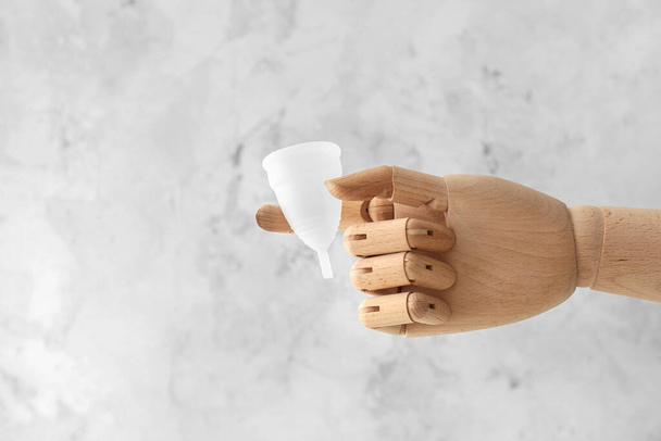 Ξύλινο χέρι με εμμηνορροϊκό κύπελλο στο φως grunge φόντο - Φωτογραφία, εικόνα