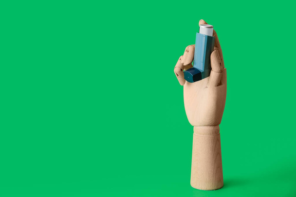 Wooden hand with asthma inhaler on green background - Foto, imagen