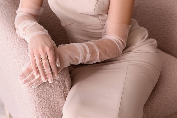 Beautiful fashionable young woman in elegant beige dress and gloves sitting in armchair, closeup - Photo, Image
