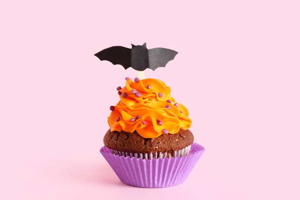 Tasty Halloween cupcake with paper bat on pink background - Fotó, kép